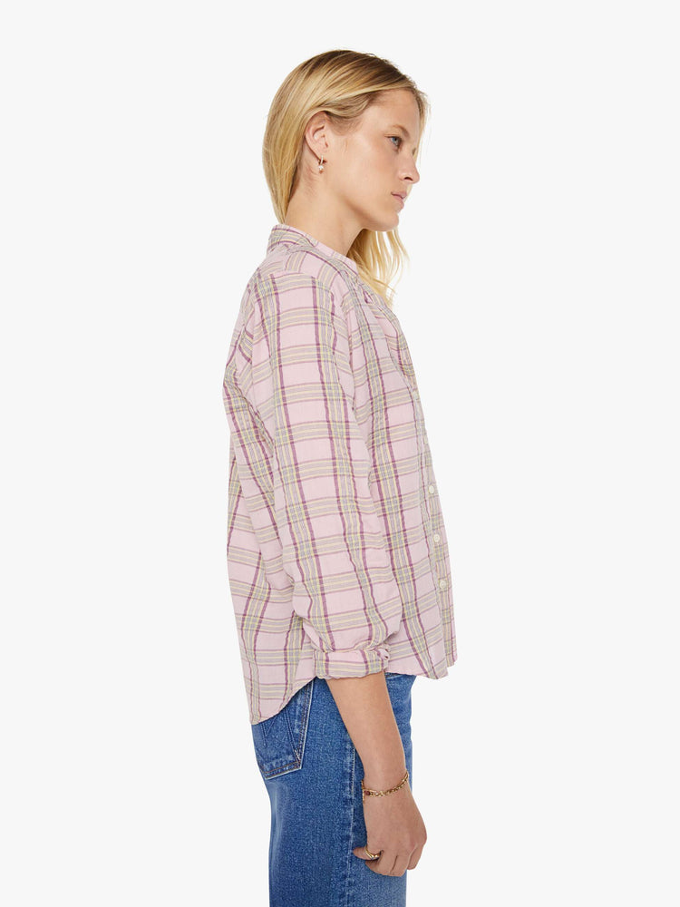 Side view of a woman in a pink plaid print shirt with elbow-length sleeves, a curved hem and a loose fit.