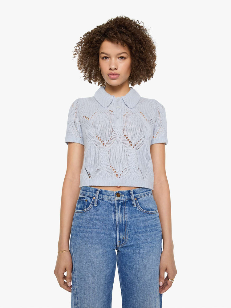 Front view of a woman in a light blue-grey top  designed with short sleeves, a collared V-neck that buttons, ribbed hems and a cable knit pattern.