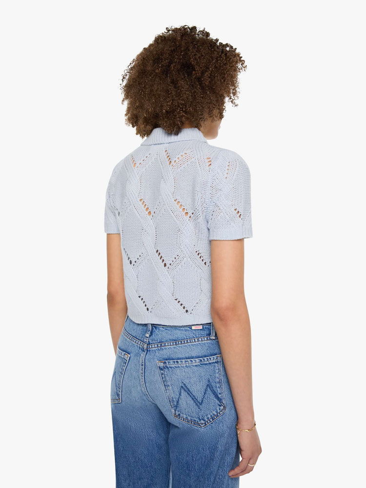 Back view of a woman in a light blue-grey top  designed with short sleeves, a collared V-neck that buttons, ribbed hems and a cable knit pattern.