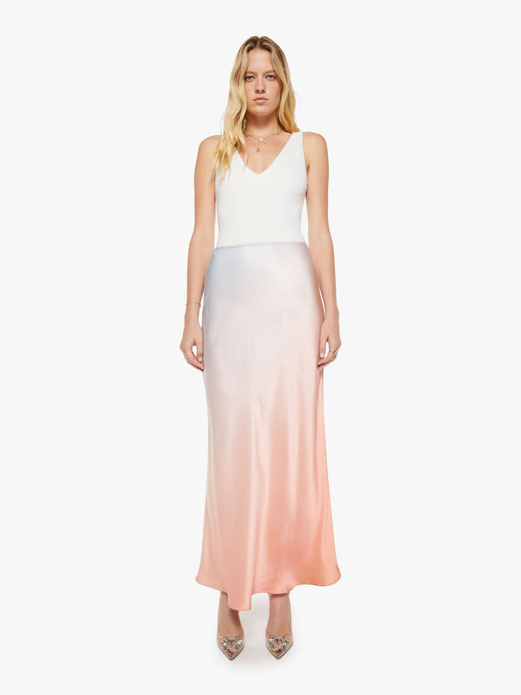 Front view of a woman in a sky blue and melon pink ombre bias cut maxi skirt is designed with a straight fit and a flowy ankle-grazing hem.