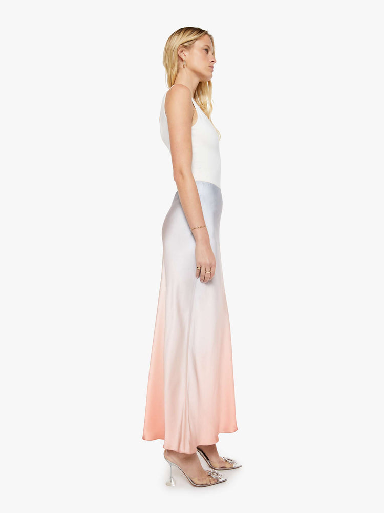 Side view of a woman in a sky blue and melon pink ombre bias cut maxi skirt is designed with a straight fit and a flowy ankle-grazing hem.