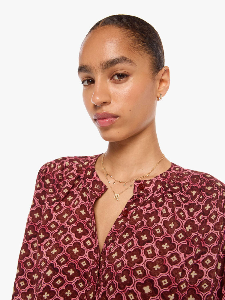 Close up view of a woman in a brick red mosaic print with a crew neck, long balloon sleeves and ruffles throughout for a flowy fit.