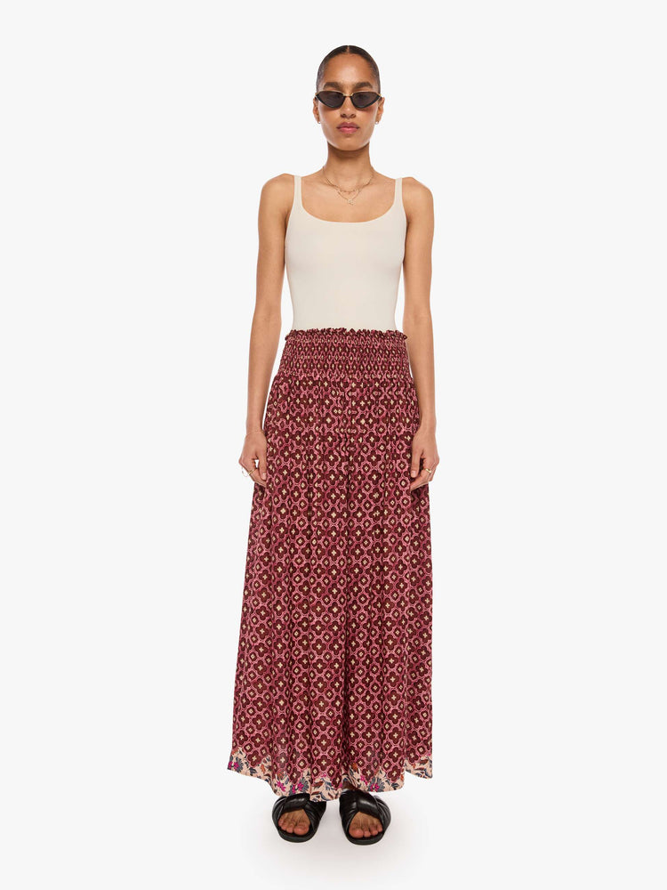 Front view of a woman in a brick red mosaic print, the skirt has a smocked waistband and a loose, flowy fit.