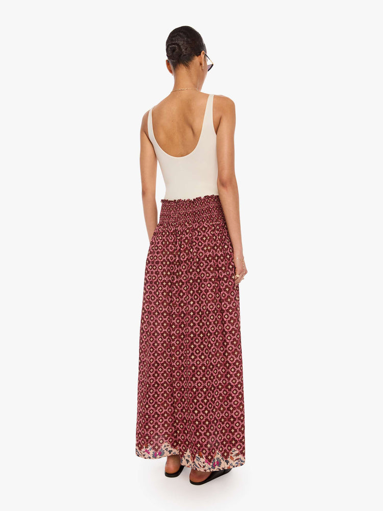 Back view of a woman in a brick red mosaic print, the skirt has a smocked waistband and a loose, flowy fit.