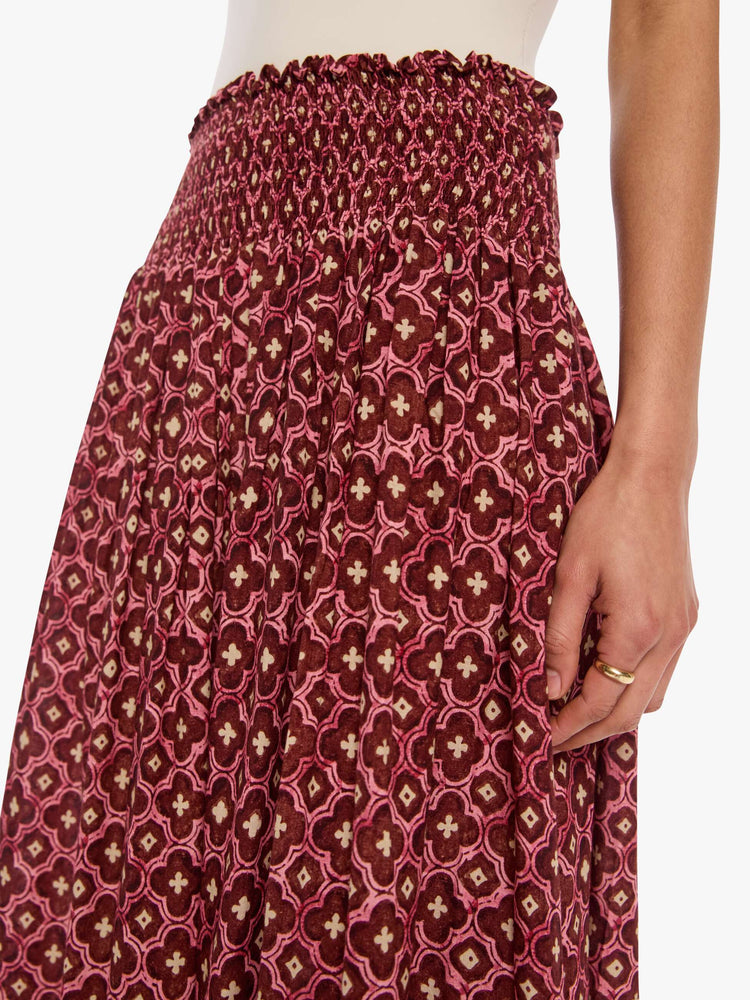 Close up view of a woman in a brick red mosaic print, the skirt has a smocked waistband and a loose, flowy fit.