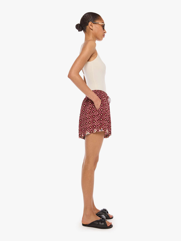 Side view of a woman in shorts with an elastic waist, side slit pockets, a slightly curved hem and loose, flowy fit.