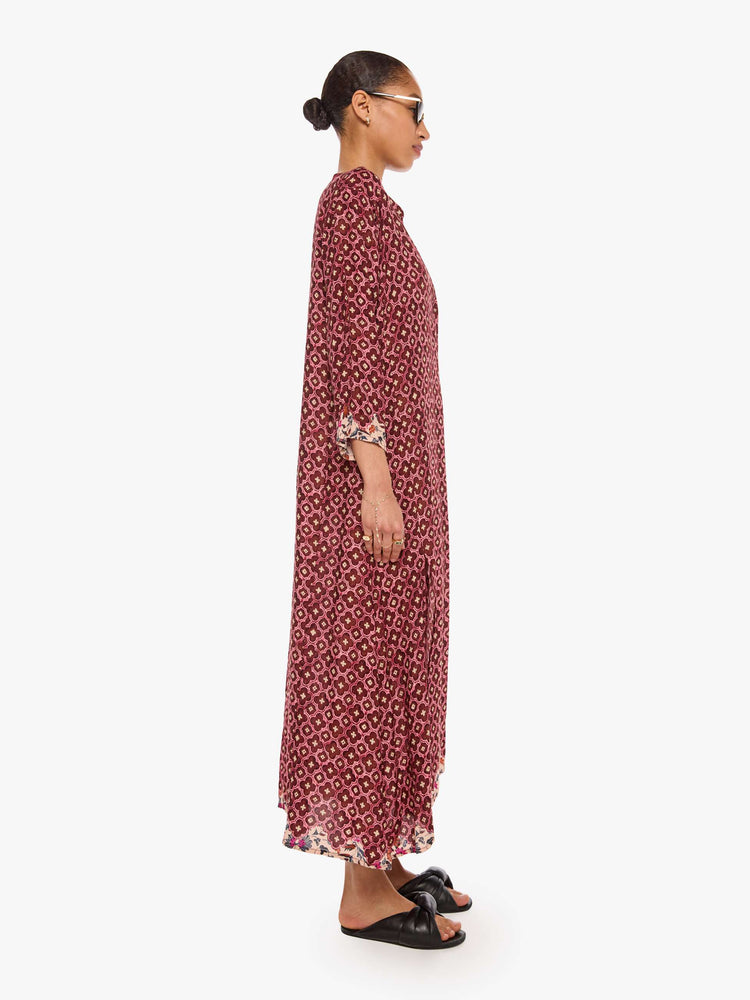 Side view of a woman in a brick red mosaic print flowy dress is designed with a deep V-neck, 3/4 sleeves and thigh-high side slits.