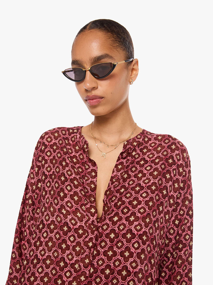 Close up view of a woman in a brick red mosaic print flowy dress is designed with a deep V-neck, 3/4 sleeves and thigh-high side slits.