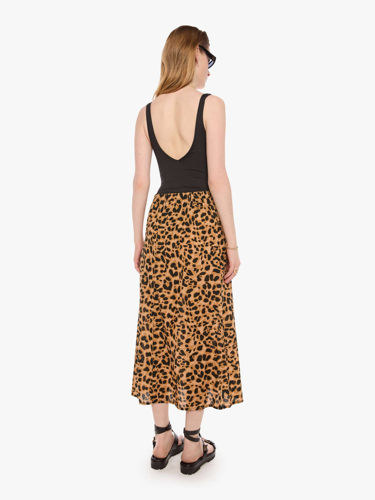 Back view of a woman in a leopard skirt with a high rise, calf-length hem and a loose, flowy fit.