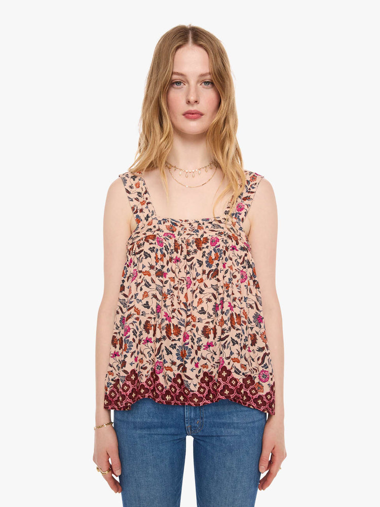 Front view of a woman in a cream with a warm-toned floral print top features detailed straps and buttons in the back.