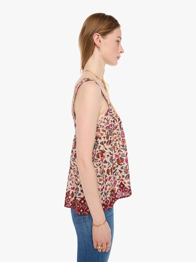 Side view of a woman in a cream with a warm-toned floral print top features detailed straps and buttons in the back.
