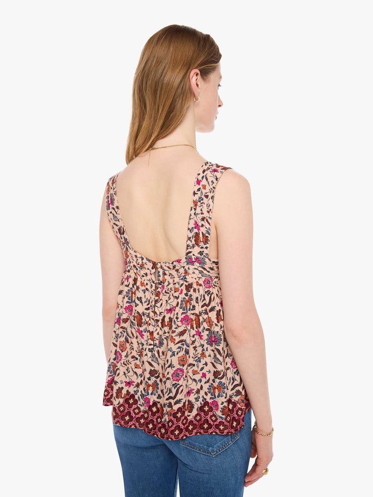 Back view of a woman in a cream with a warm-toned floral print top features detailed straps and buttons in the back.