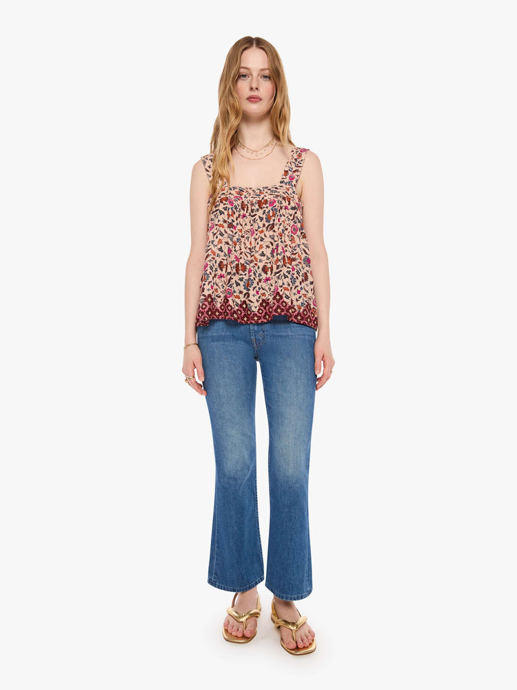 Full body view of a woman in a cream with a warm-toned floral print top features detailed straps and buttons in the back.