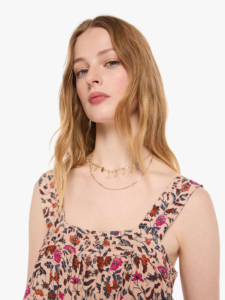Close up view of a woman in a cream with a warm-toned floral print top features detailed straps and buttons in the back.