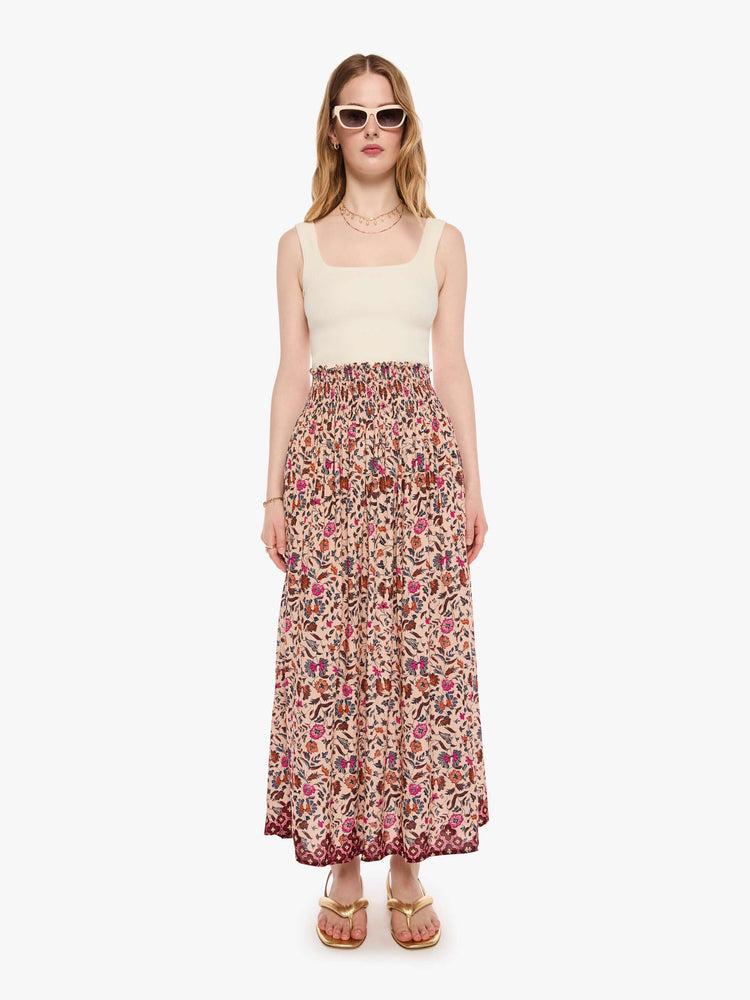 Front view of a woman in a cream with a warm-toned floral print, the skirt has a smocked waistband and a loose, flowy fit.