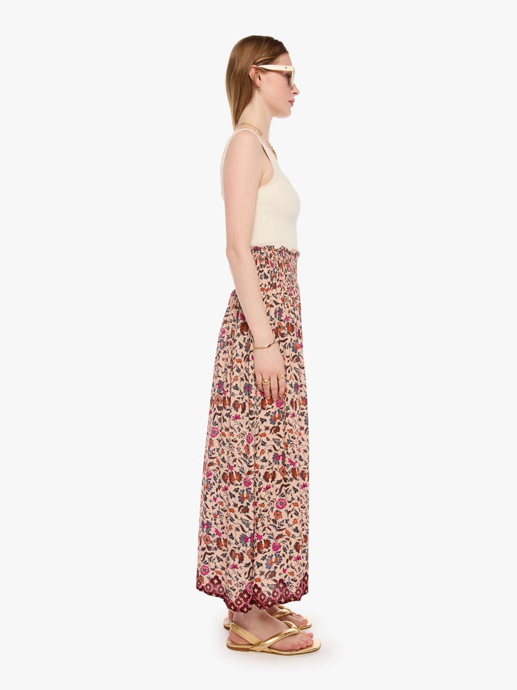 Side view of a woman in a cream with a warm-toned floral print, the skirt has a smocked waistband and a loose, flowy fit.