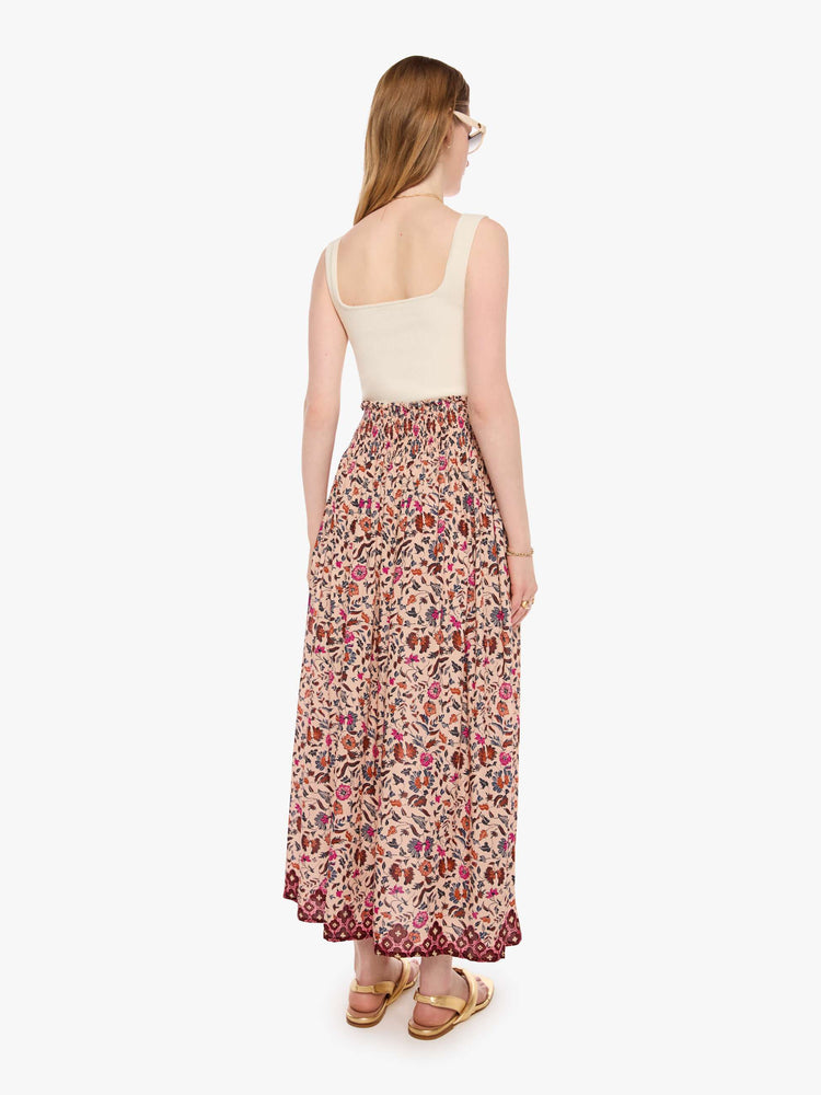 Back view of a woman in a cream with a warm-toned floral print, the skirt has a smocked waistband and a loose, flowy fit.