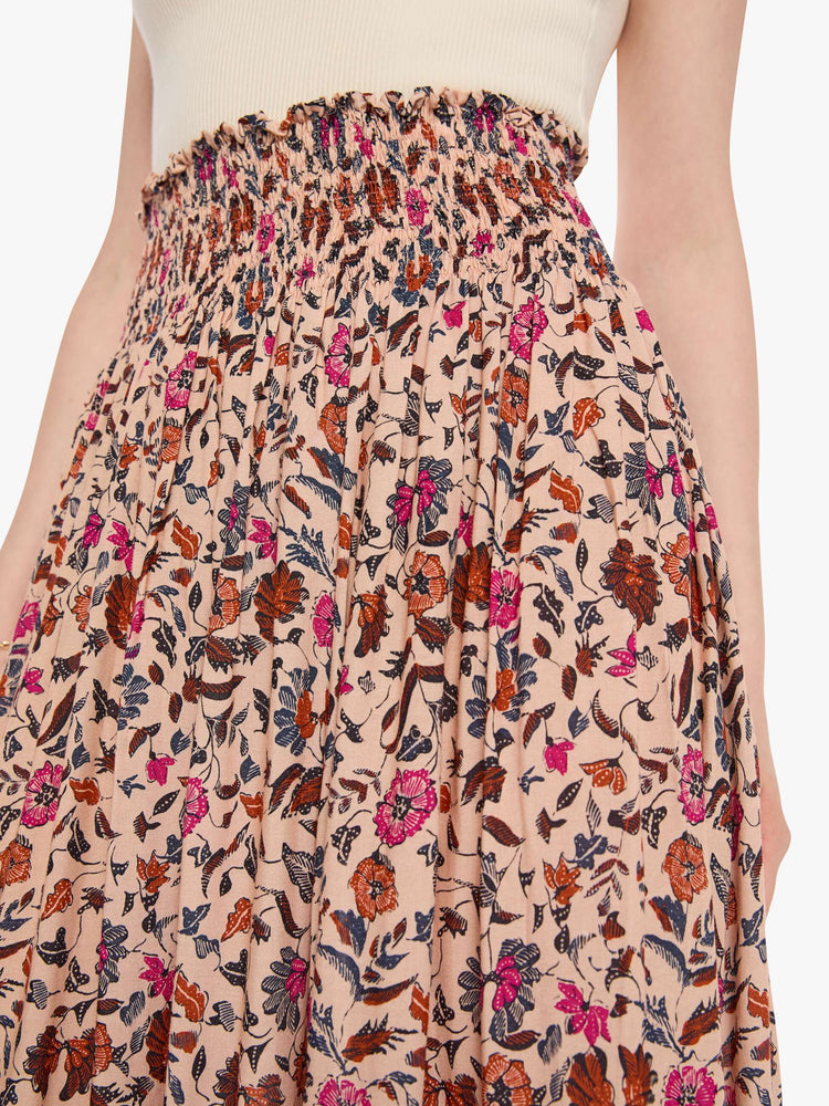 Close up view of a woman in a cream with a warm-toned floral print, the skirt has a smocked waistband and a loose, flowy fit.