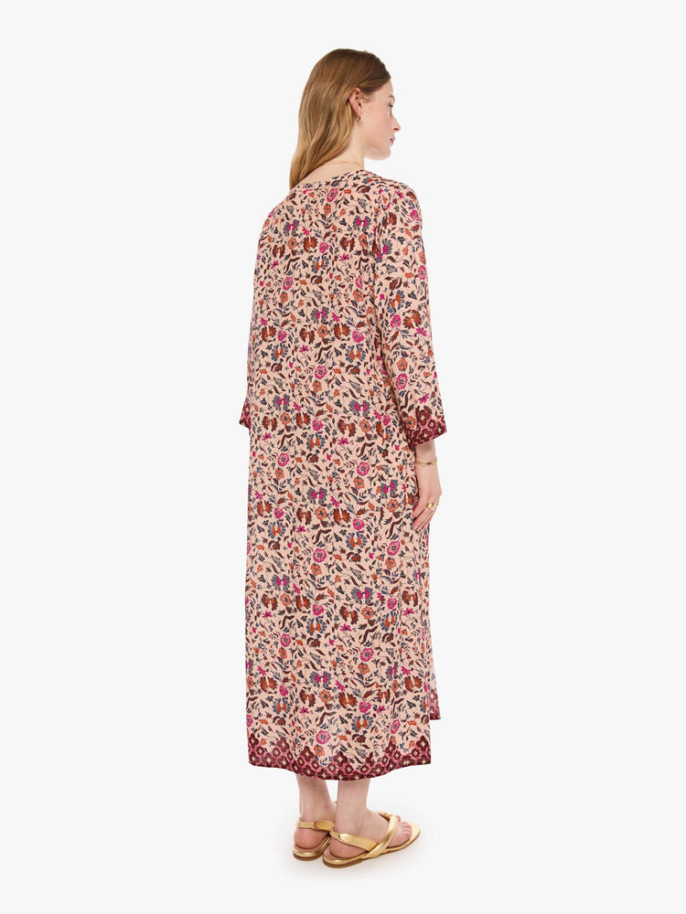 Back view of a woman in cream with a warm-toned floral print flowy dress has a deep V-neck, 3/4 sleeves and thigh-high side slits.