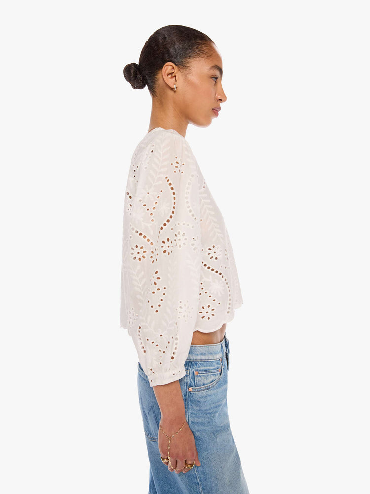 Side view of a woman in a white top with embroidery and eyelet details, and features a crewneck, 3/4-length balloon sleeves, a slightly cropped scalloped hem and a boxy fit.