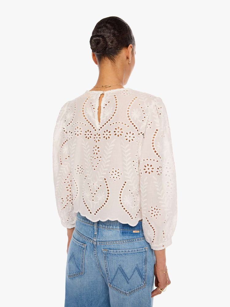 Back view of a woman in a white top with embroidery and eyelet details, and features a crewneck, 3/4-length balloon sleeves, a slightly cropped scalloped hem and a boxy fit.