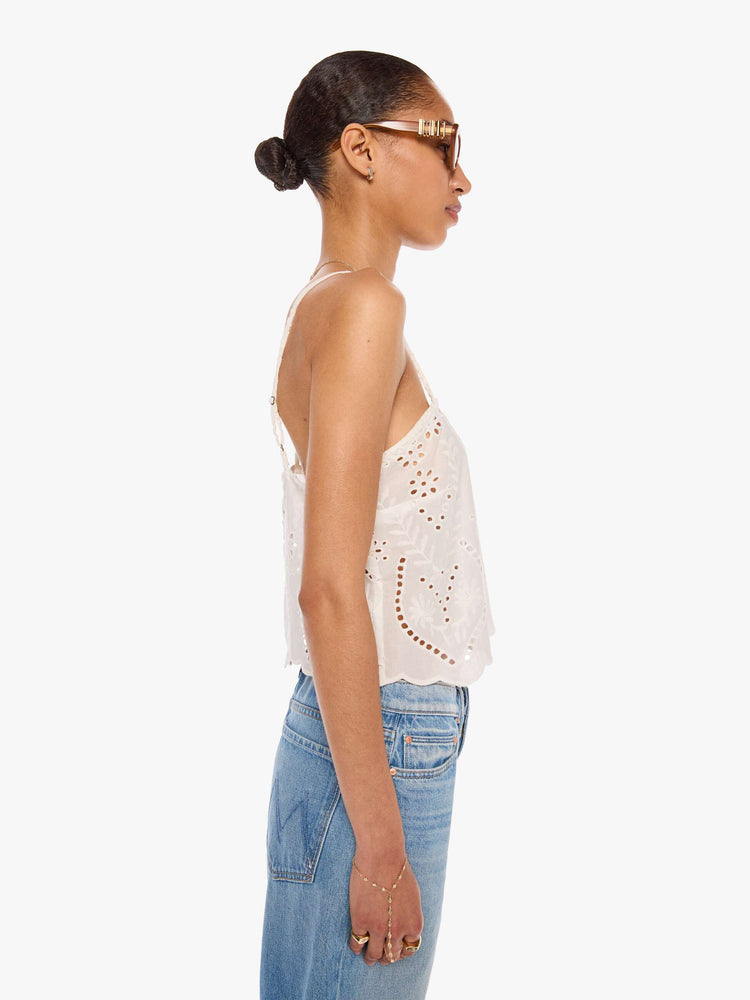 Side view of a woman in an off-white with delicate embroidery, eyelet details and a scalloped hem, the Fern cami has a square neck, spaghetti straps and a cropped, boxy fit.