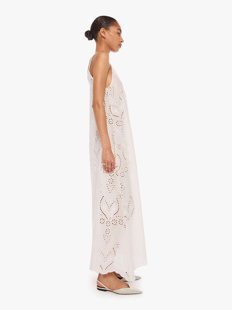 Side view of a woman in a dress with a scoop neck, thin spaghetti straps, an ankle-length hem and a loose, flowy fit.