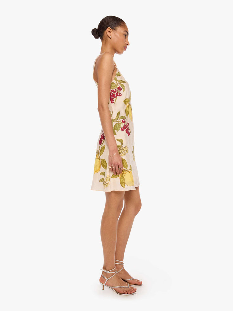 Side view of a woman in a  sleeveless Addie dress is made from 100% silk in cream with an oversized fruit print, and features a scoop neck, narrow fit and short hem.