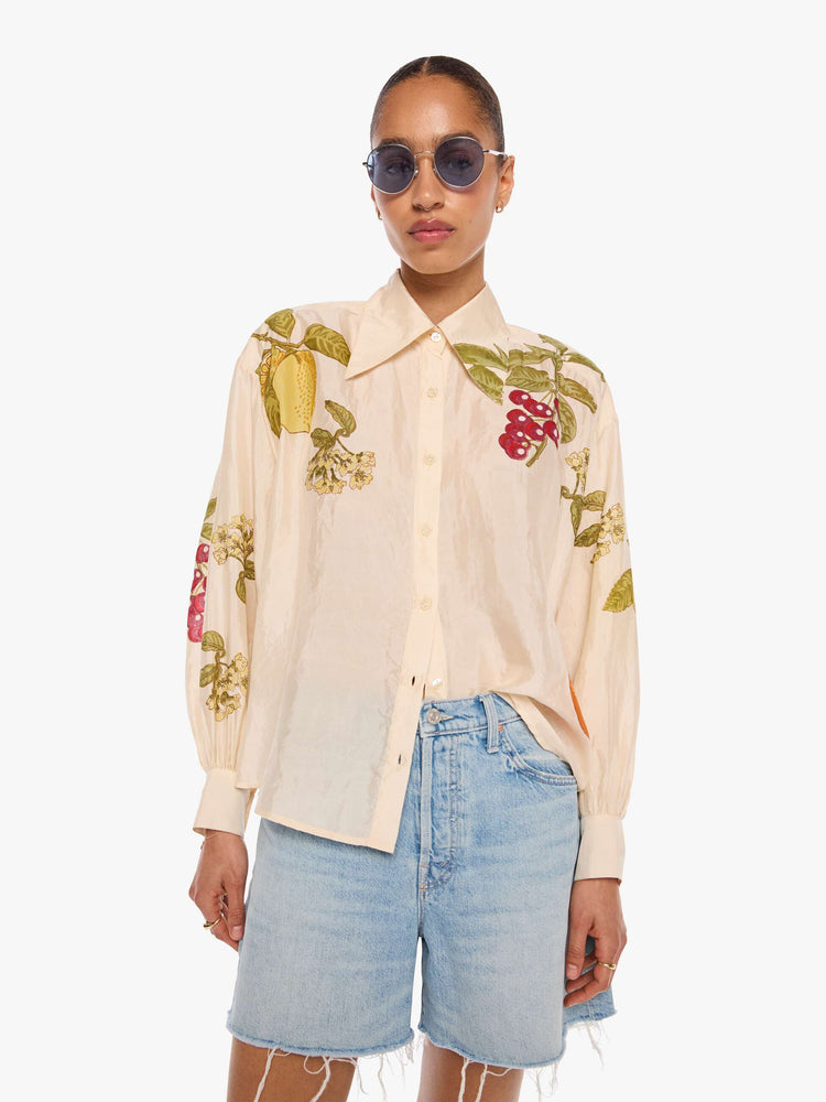 Front view of a woman in a cream with an oversized fruit print shirt and features drop shoulders, long sleeves, curved hems and buttons down the front.