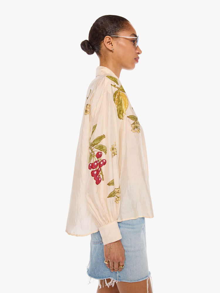 Side view of a woman in a cream with an oversized fruit print shirt and features drop shoulders, long sleeves, curved hems and buttons down the front.