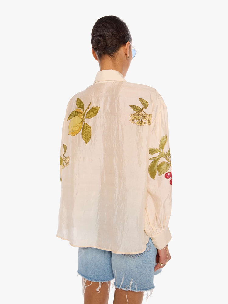 Back view of a woman in a cream with an oversized fruit print shirt and features drop shoulders, long sleeves, curved hems and buttons down the front.