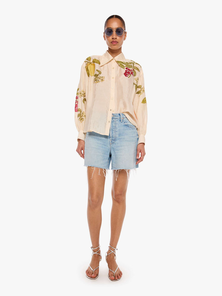 Full body view of a woman in a cream with an oversized fruit print shirt and features drop shoulders, long sleeves, curved hems and buttons down the front.