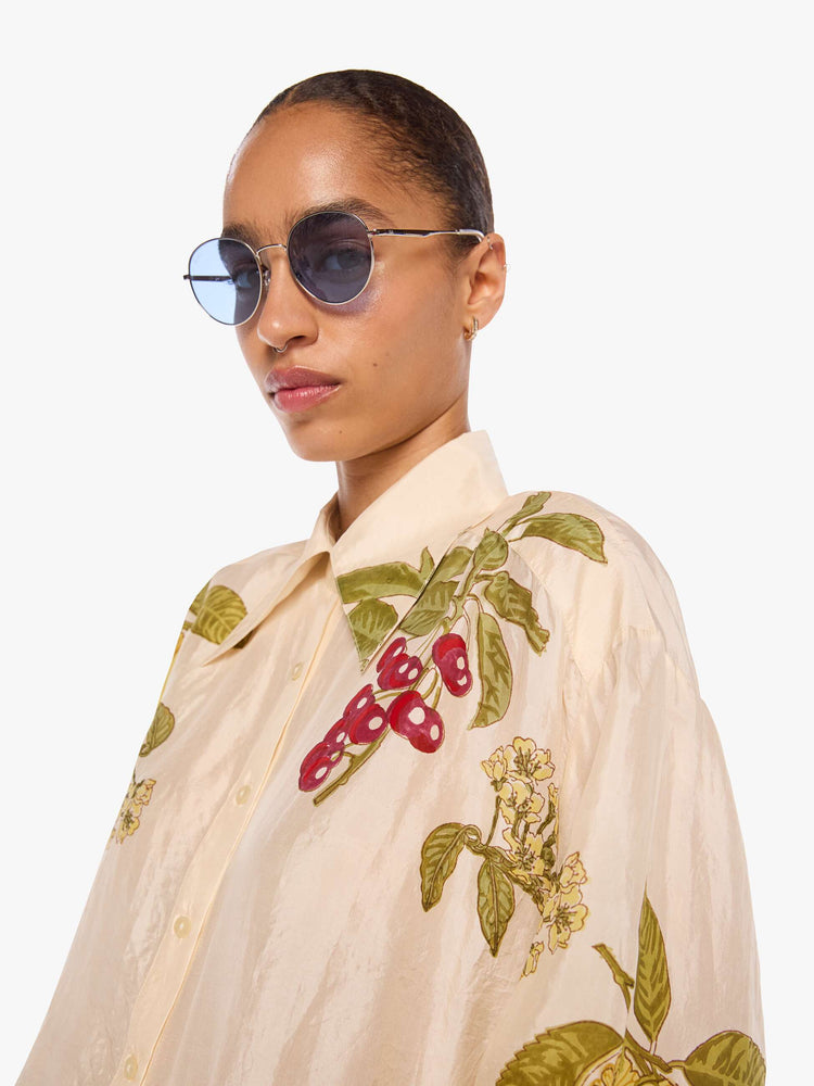 Close up view of a woman in a cream with an oversized fruit print shirt and features drop shoulders, long sleeves, curved hems and buttons down the front.