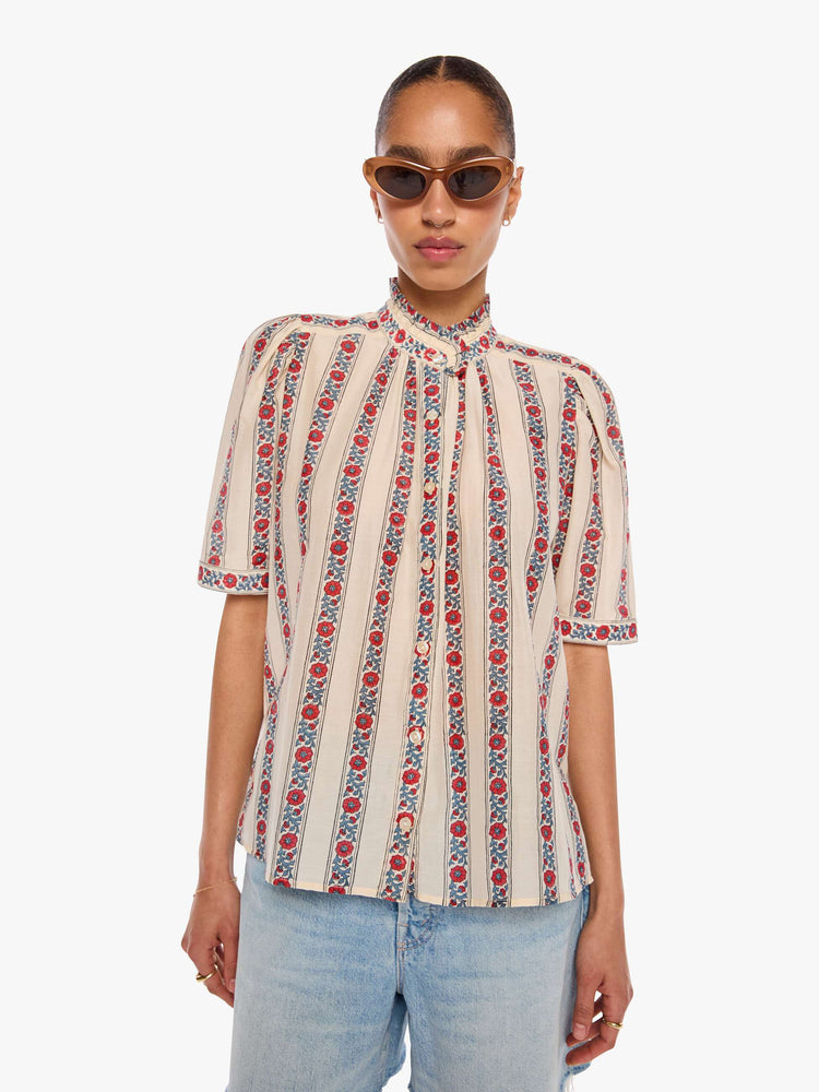 Front view of a woman in a silk cream with light blue stripes detailed with roses shirt with a stacked collar, elbow-length sleeves, buttons down the front and a curved hem.
