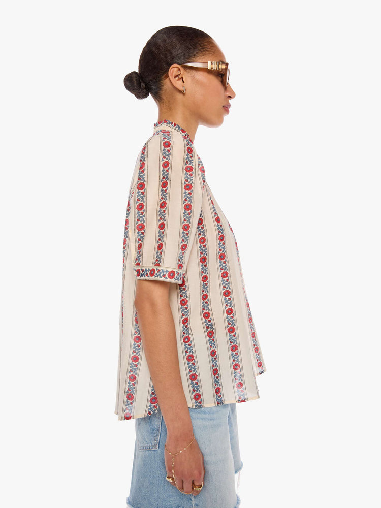 Side view of a woman in a silk cream with light blue stripes detailed with roses shirt with a stacked collar, elbow-length sleeves, buttons down the front and a curved hem.