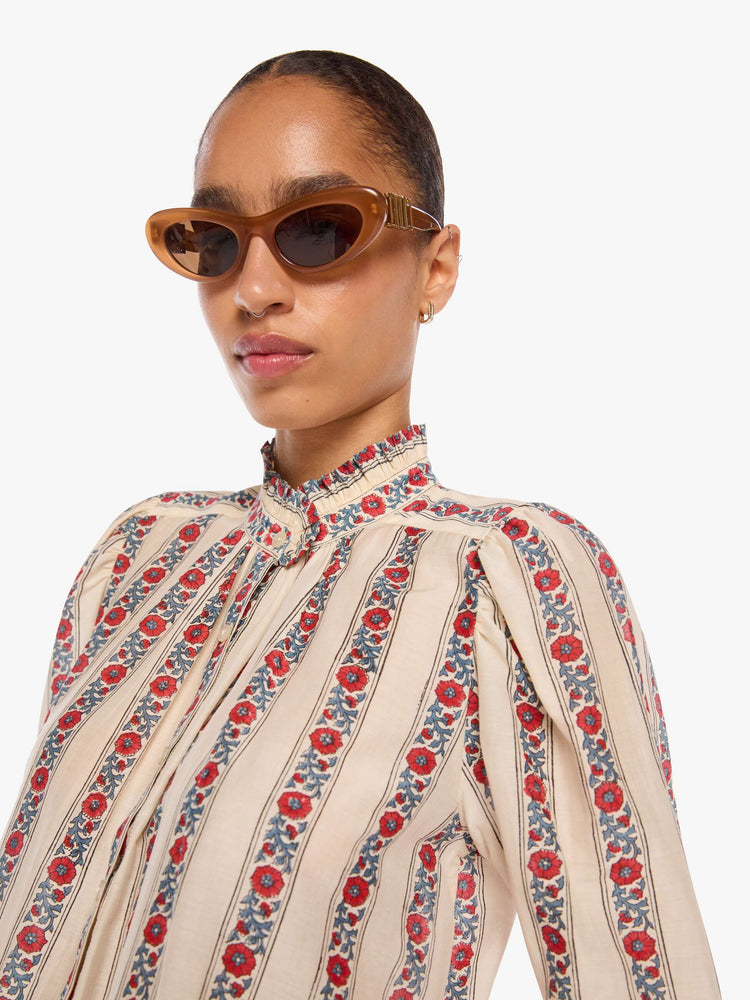 Clos up view of a woman in a silk cream with light blue stripes detailed with roses shirt with a stacked collar, elbow-length sleeves, buttons down the front and a curved hem.