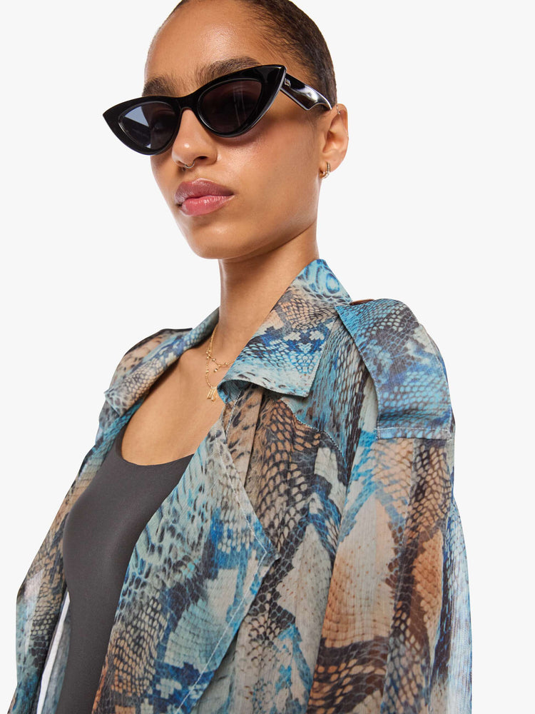Close up view of a woman in a blue, cream, brown and black oversized snake print jacket and features a notched collar, long sleeves and an ankle-length hem.