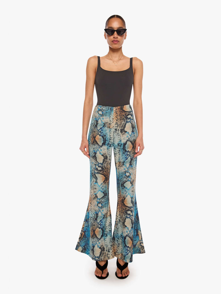 Front view of a woman in a pant with a blue, cream, brown and black oversized snake print, and features a high rise and a loose, flared leg.