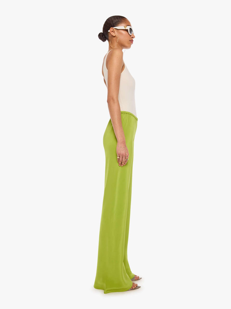 Side view of a woman in a green pant with an elastic waistband, a loose leg and an extra-long hem.