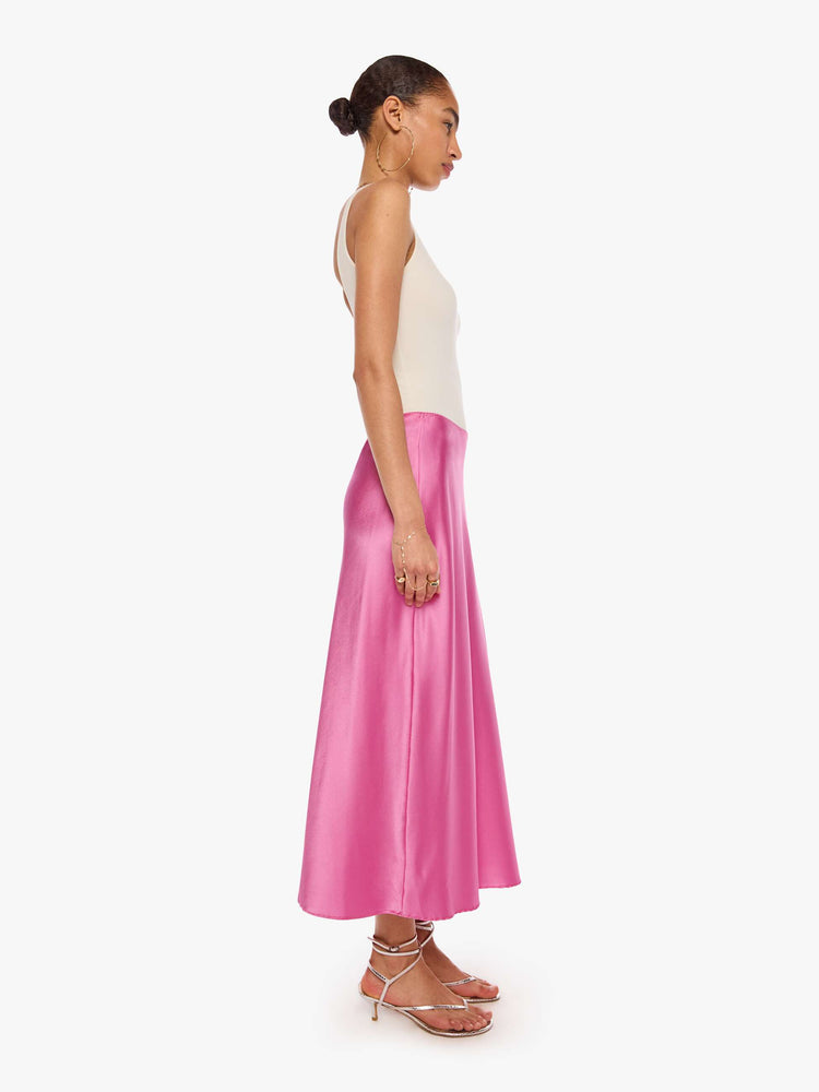 Side view of a woman in a pink bias-cut maxi skirt is designed with a straight fit and a flowy, ankle-grazing hem.