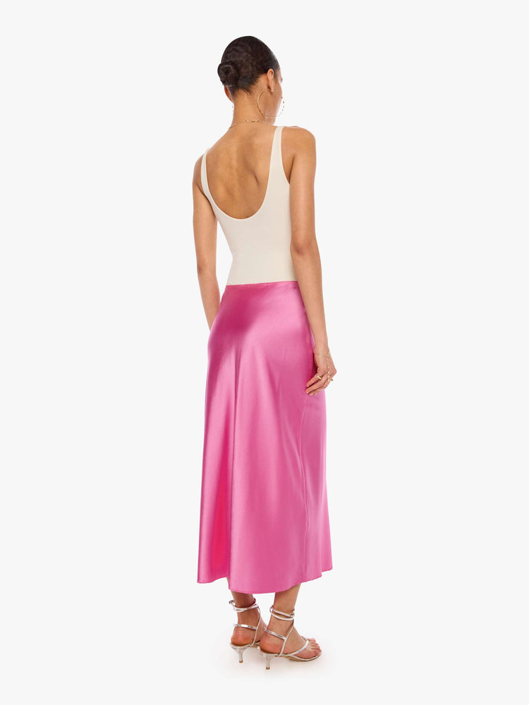 Back view of a woman in a pink bias-cut maxi skirt is designed with a straight fit and a flowy, ankle-grazing hem.