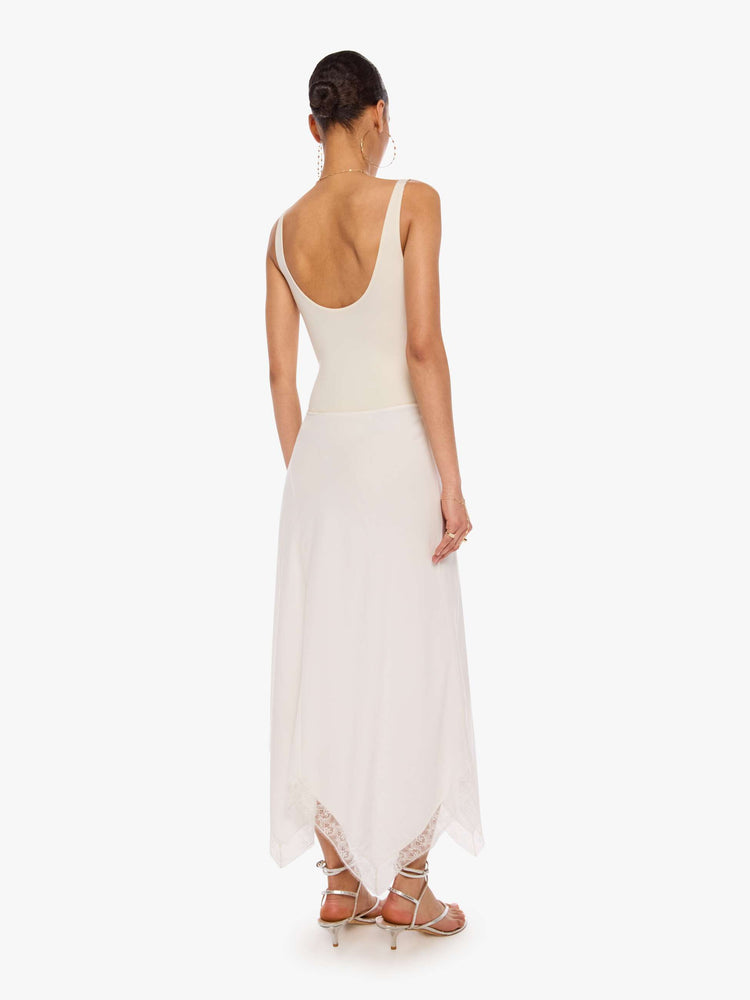 Back view of a woman in a white bias-cut maxi skirt features a flowy fit and an ankle-length uneven hem with lace trim.