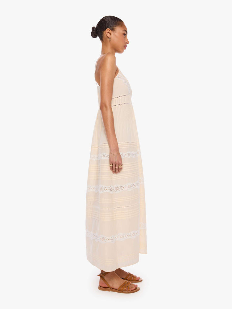 Side  view of a woman in off white  thin spaghetti straps dress and a V-neck, fitted bodice and a flowy skirt. 