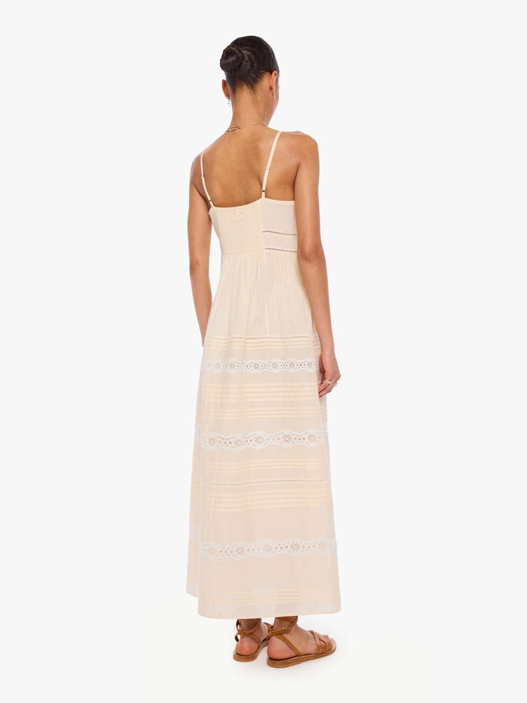Back  view of a woman in off white  thin spaghetti straps dress and a V-neck, fitted bodice and a flowy skirt. 