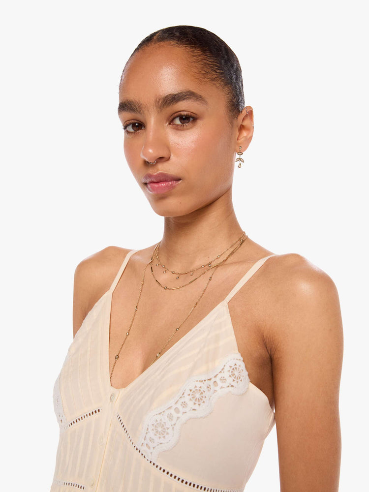 Close up  view of a woman in off white  thin spaghetti straps dress and a V-neck, fitted bodice and a flowy skirt. 