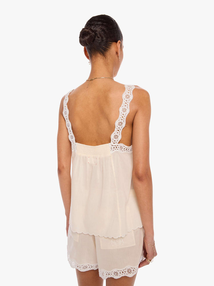 Back view of a woman in an off-white  shirt with pleats, embroidery and eyelet details on the chest and straps and a scalloped hem.