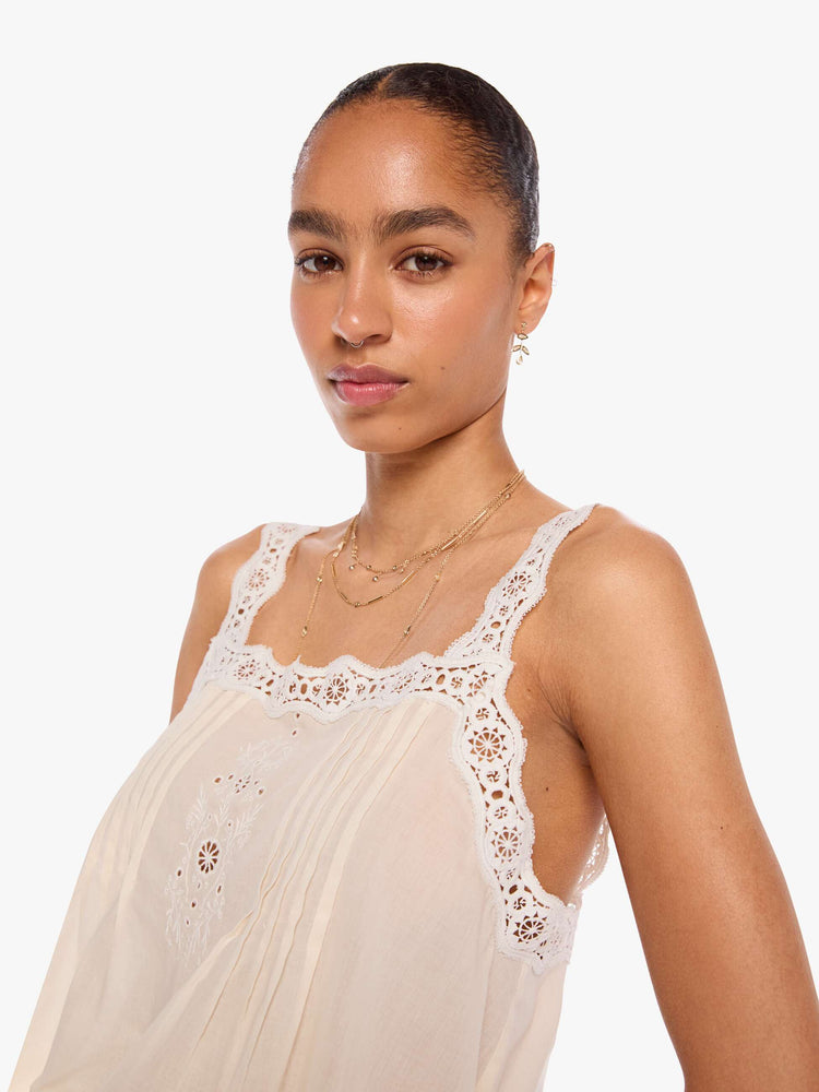 Close up view of a woman in an off-white  shirt with pleats, embroidery and eyelet details on the chest and straps and a scalloped hem.