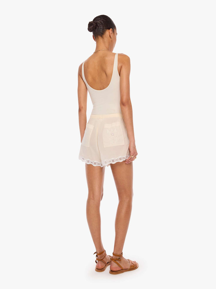 Back view of a woman in off-white short with pleats, embroidery, eyelet details and a scalloped hem.