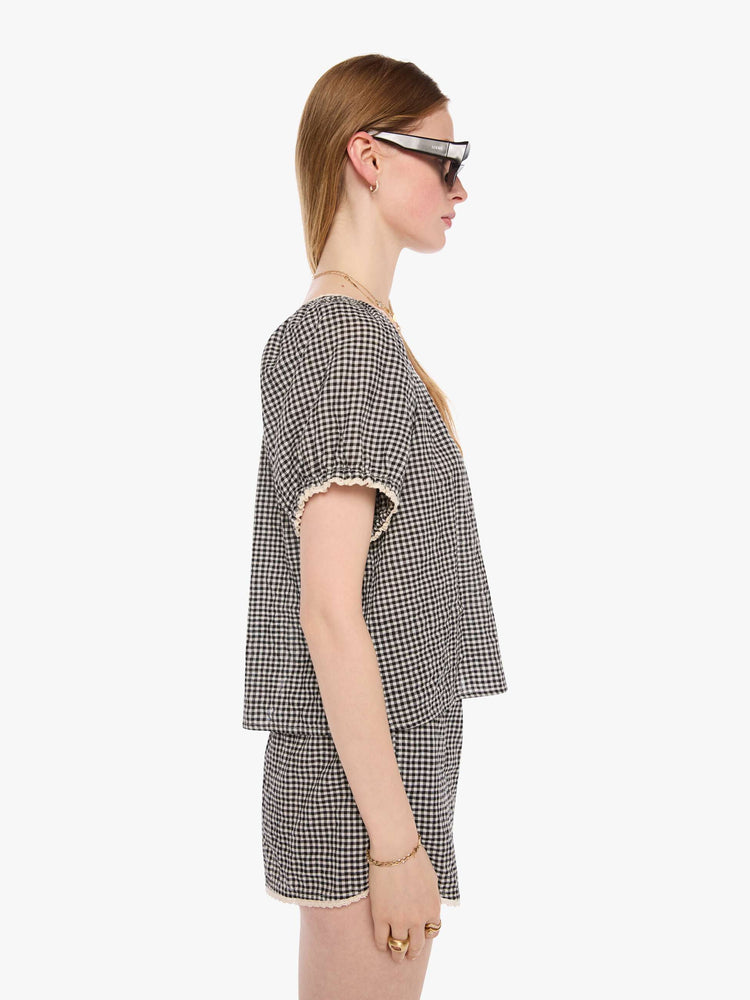Side view of a woman in a black and off white shirt with a scoop neck, oversized balloon sleeves and pleats throughout for a loose, flowy fit.