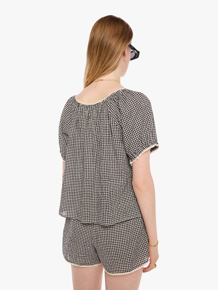 Back view of a woman in a black and off white shirt with a scoop neck, oversized balloon sleeves and pleats throughout for a loose, flowy fit.